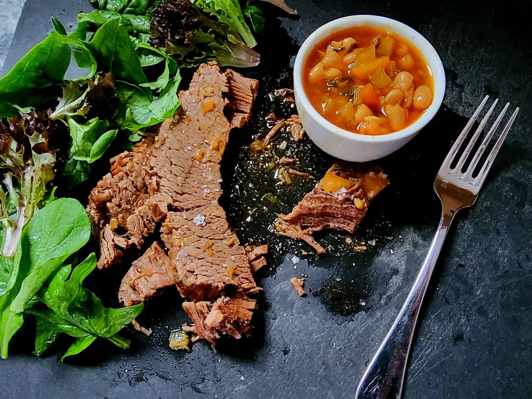 Brisket slices on a board with White Beans, greens + a fork
