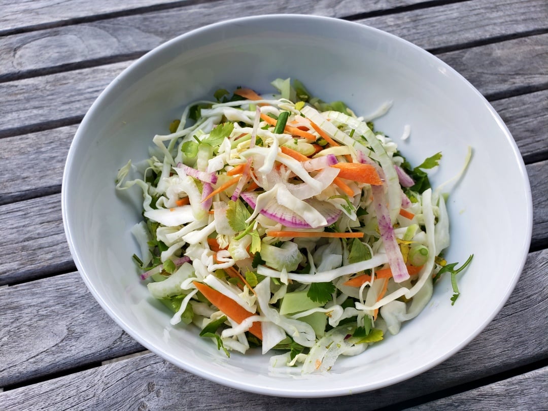 Cabbage, Bok Choy & Radish Salad in a white bowl on a teak table
