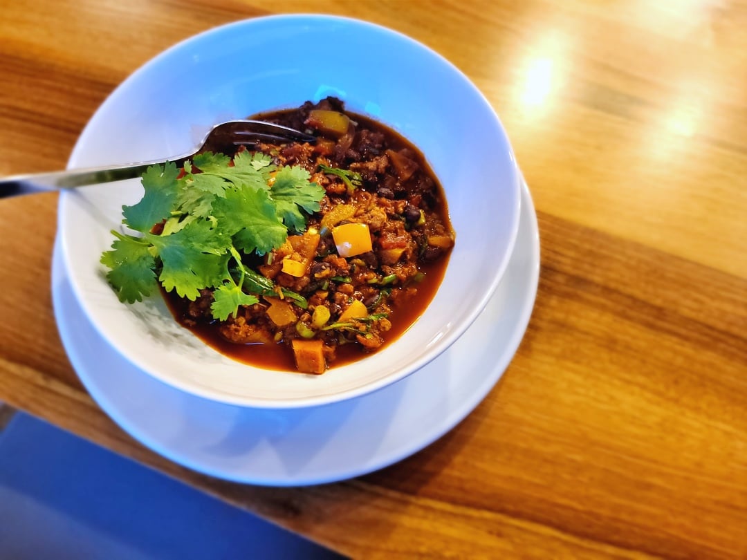 Turkey Veggie Chilli in a bowl on a plate with cilantro garnish + fork